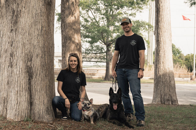 Two trainers posing with their dogs among trees