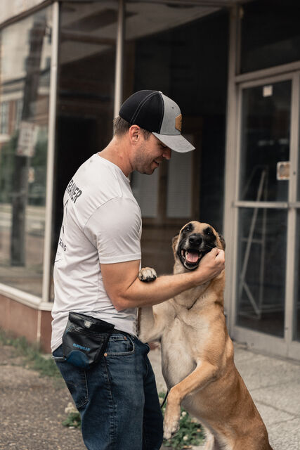 Trainer holding a tan dog close outside a storefront