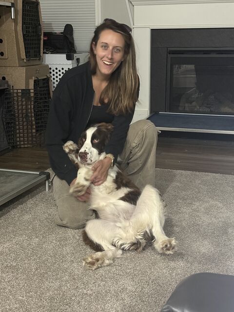 Smiling woman kneeling on a rug with a brown-and-white dog resting against her